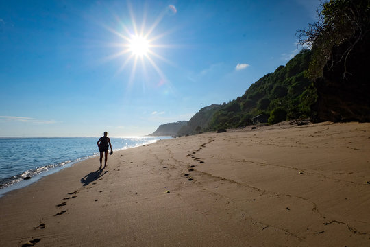 Man walking along a lonely beach with bright blue sky and shining sun