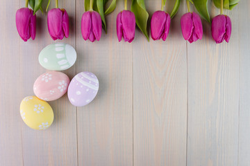 Easter painted eggs on wooden light background with spring pink bouquet tulips. Empty space for text. Top view.