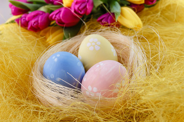 Easter painted eggs in the nest on yellow straw with spring bouquet yellow and magenta tulips.