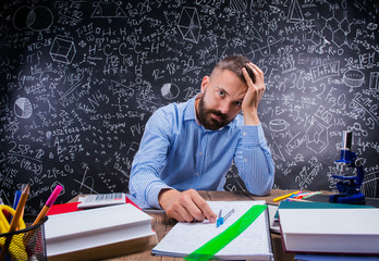 Upset teacher at desk, school supplies, holding head, blackboard
