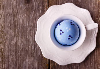 Easter blue painted egg in the white cup on wooden rustic background. Empty space for text.