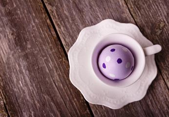 Easter violet painted egg in the white cup on wooden rustic background. Empty space for text.