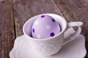 Easter painted violet egg in white cup on wooden rustic background.