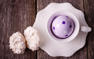 Easter painted violet egg in white cup with coconut cookies on wooden rustic background.
