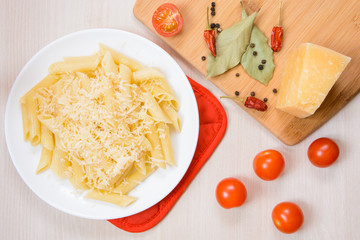 Penne pasta with grated cheese on a white round plate next to the spices and tomatoes on the table