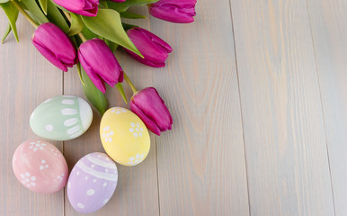 Easter painted eggs on wooden light background with spring pink bouquet tulips. Empty space for text. Top view.