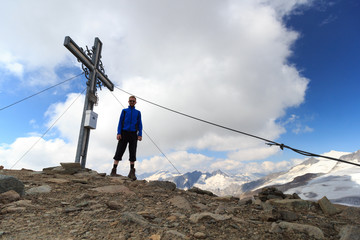 Summit cross and male mountaineer on mountain Weißspitze with panorama in Hohe Tauern Alps, Austria