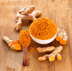 fresh turmeric roots with turmeric powder on wooden table