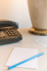 Telephone, pencil and blank white paper on hotel room