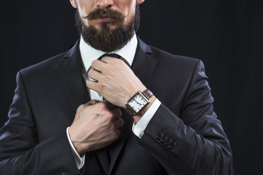 Elegant bearded man in suit correcting his tie. Preparation for work.