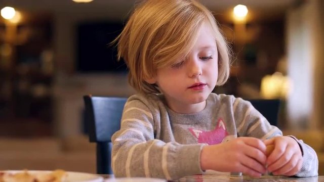 A little girl eating crackers at the kitchen counter, with bokeh behind her, slow motion