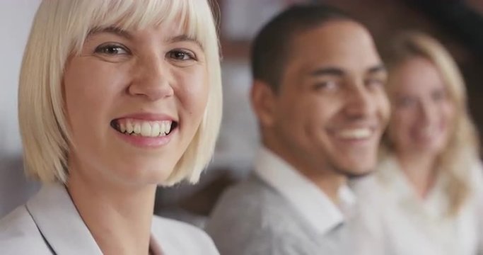 Portrait of a confident young business woman at boardroom table in trendy modern shared office space a diverse team chatting together slow motion turning around smiling
