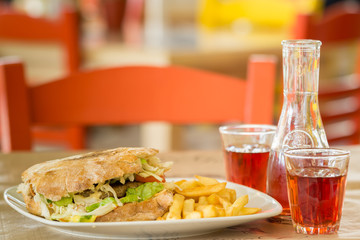 Hamburger of Italian bread with a big steak .Grafin and two glasses of wine. In the tavern in Greece