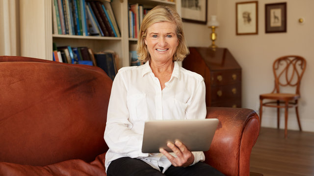 Smiling senior woman in living room with digital tablet