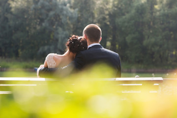 Bride and groom sitting together on bench outdoors. Rear view