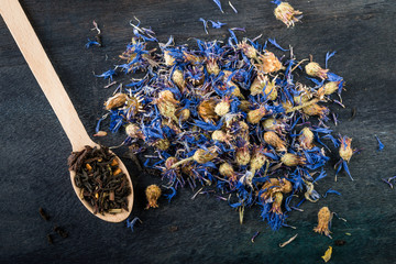  Dried cornflower tea on wooden spoon  on dark  table.