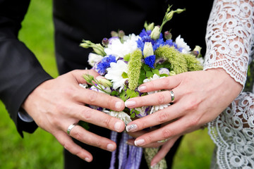 Hands with wedding rings on bride's bouquet