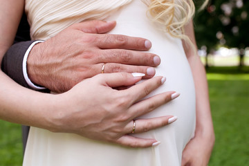 Hands with wedding rings on pregnant belly