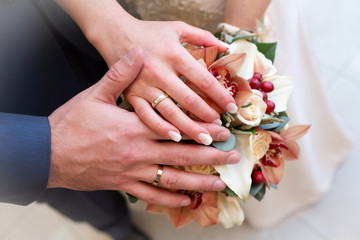 Hands with wedding rings on bride's bouquet