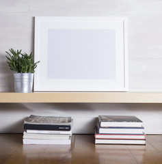 A white picture frame sitting on a wooden shelf with plant and books.