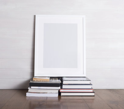 A white picture frame sitting on top of two piles of books