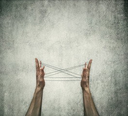 Two human hands playing cats cradle game with a thread on a grey concrete background. Creative...
