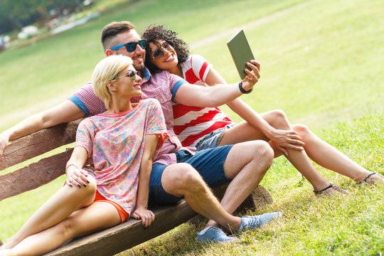Two best female friends using tablet and doing selfie in park.