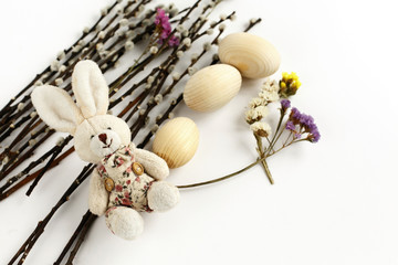 cute rabbit and willow branches with buds and wooden eggs on whi