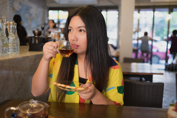 Woman is drinking hot tea /Woman in colorful dress is drinking and sipping hot tea in coffee shop