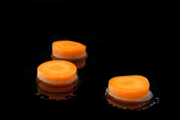 drei scheiben karotte mit wasser auf schwarzen hintergrund