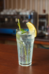 highball glass with ice and a yellow tube on the wooden bar
