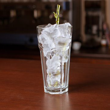 highball glass with ice and a yellow tube on the wooden bar