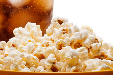Salted popcorn grains in the dish and a glass of cola on the whi