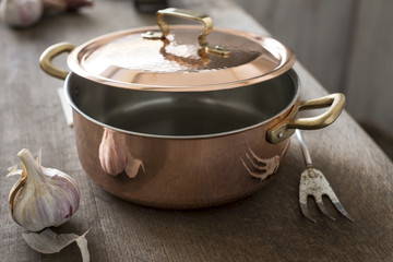 Partially Covered Copper Cooking Pot Between Garlic and Carving