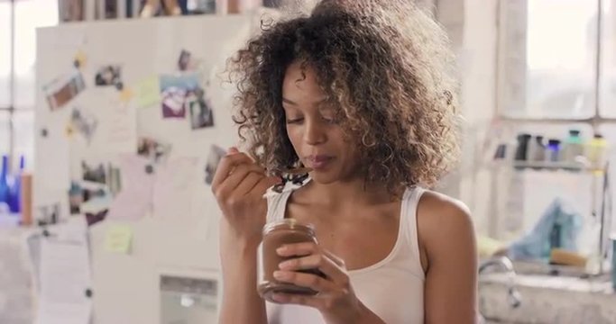 Mixed race girl indulging eating chocolate spread from  jar using spoon