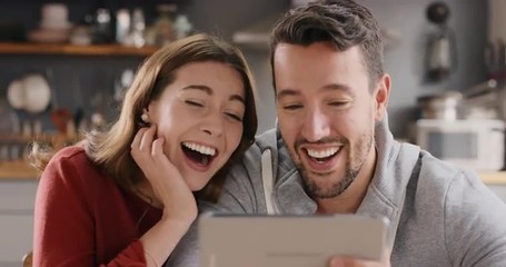 Attractive young couple at home laughing at funny internet joke online using digital tablet - Powered by Adobe