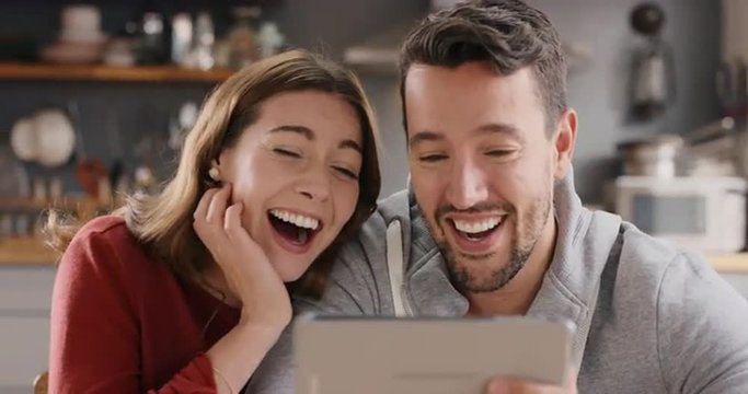 Attractive young couple at home laughing at funny internet joke online using digital tablet