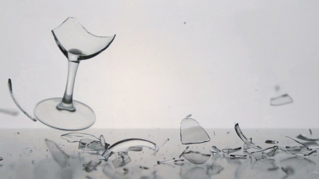 SLOW: A clear winegalss falls and breaks on a white table
