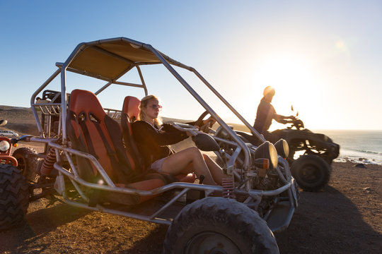 Active woman driving quadbike on dirt road by the sea in sunset. - Powered by Adobe