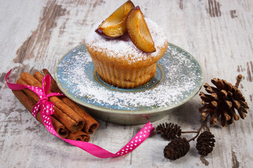 Muffins with plums and powdered sugar, cinnamon sticks on old wooden background, delicious dessert