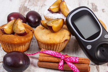 Glucometer, muffins with plums and cinnamon sticks on wooden background, diabetes and delicious dessert