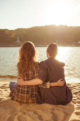 Young man and woman sitting at the beach and huging each other