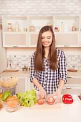 Attractive cheerful young woman cutting tomatoes for salad