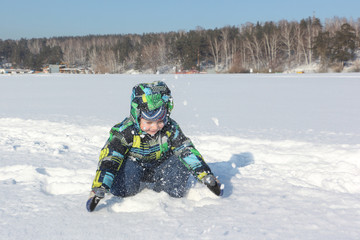 Fototapeta na wymiar The little boy in a color jacket with a hood throws snow during a winter entertainment up 
