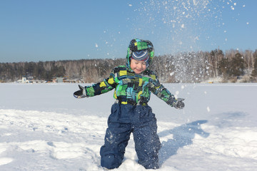 The little boy in a color jacket with a hood throws snow during a winter entertainment up

