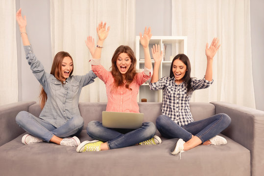 Three successful happy girls sitting on the couch with laptop