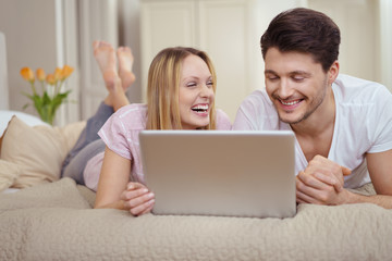 lachendes paar liegt auf dem bett und schaut ein lustiges video am laptop