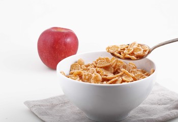 corn and rice flakes in white bowl and red Apple