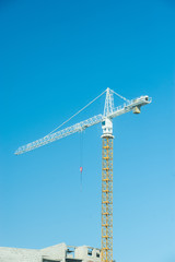 Construction crane against the blue sky and building under construction