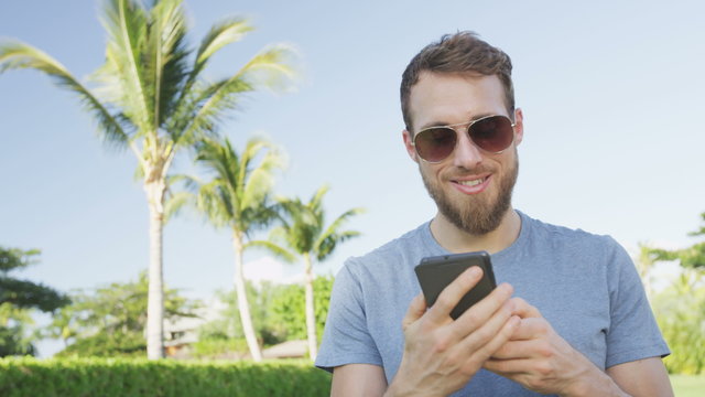 Smartphone man talking calling on smart phone outdoors in summer. Handsome young casual man using mobile cell phone smiling happy wearing sunglasses. Urban male hipster. RED EPIC 90 FPS.
